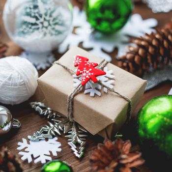 Christmas and New Year background with presents, ribbons, balls and different green decorations on wooden background. Gift packed in craft paper with red fir tree.