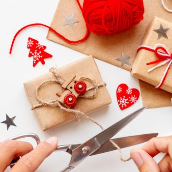 Woman wrapping DIY presents in craft paper. Christmas and New Year gifts tied with white and red threads with toy train as decoration.