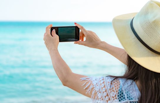 Asian hipster woman wear hat use smartphone taking photo of beautiful sea. Summer vacation at tropical paradise beach. Happy hipster girl travel on holiday. Woman enjoy and relax . Summer vibes. 