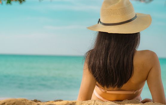 Back view of happy young Asian woman in pink swimsuit and straw hat relax and enjoy holiday at tropical paradise beach at sunset. Girl in summer vacation fashion. Beauty sexy model. Summer vibes.