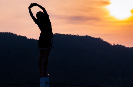 Healthy woman stretching arms and body in the morning with beautiful sunrise over the mountain. Happy young  female exercise at the park. Outdoor workout before fitness training. Active woman warm up.