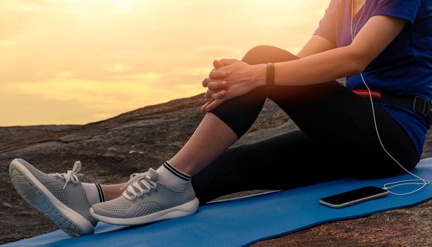 Woman sit and relax on yoga mat and listen to music via smartphone at stone beach by the sea . Woman outdoor workout. Fit girl wear smart band. Healthy, chill out lifestyle. Relax on summer vacations.