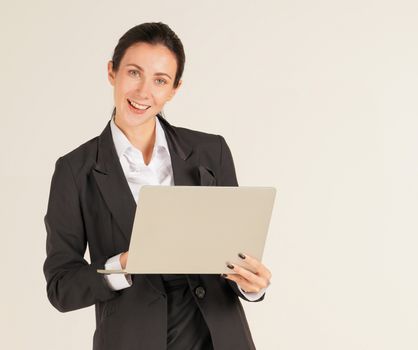 A business woman in a black suit with a smile and typing on a computer notebook. Portrait on beige background with studio light.