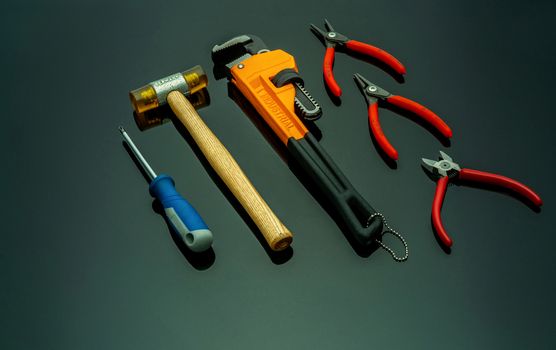 Set of mechanic tools isolated on black background. Screwdriver, red end cutter pliers, locking pliers, pincers, plastic hammer with wooden handle, and monkey pipe wrench. Tools for technician to fix.