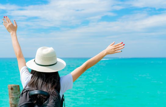 Happy young Asian woman in casual style fashion with straw hat and backpack. Relax and enjoy holiday at tropical paradise beach. Girl stand at the wood pier of resort in summer vacation. Summer vibes.