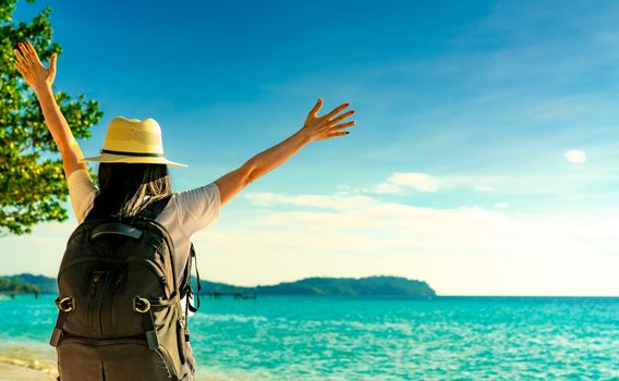 Back view of happy young Asian woman in casual style fashion with straw hat and backpack. Relax and enjoy holiday at tropical paradise beach. Summer vibes. Relaxing and enjoying at tropical beach.