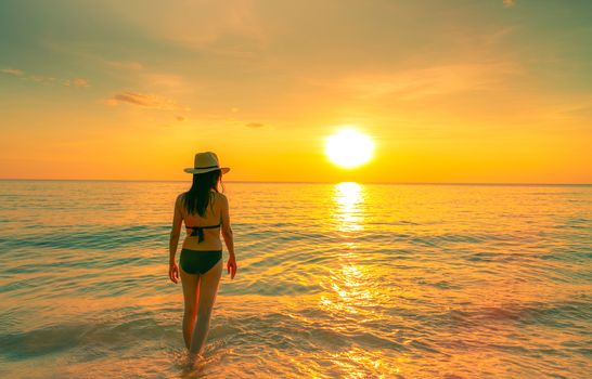 Silhouette sexy woman walking at tropical sea with beautiful sunset sky at paradise beach. Happy girl wear bikini and straw hat relaxing summer vacation. Holiday travel. Summer vibes. Life goes on.