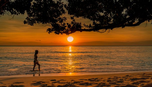 Silhouette sexy woman walking at tropical sea with beautiful sunset sky at paradise beach. Happy girl wear bikini and straw hat relaxing summer vacation. Holiday travel. Summer vibes. Life goes on.