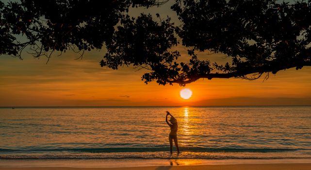Silhouette back view of sexy woman watching beautiful sunset at tropical paradise beach. Happy girl wear bikini and straw hat relaxing summer vacation. Holiday travel. Summer vibes. Peaceful life.