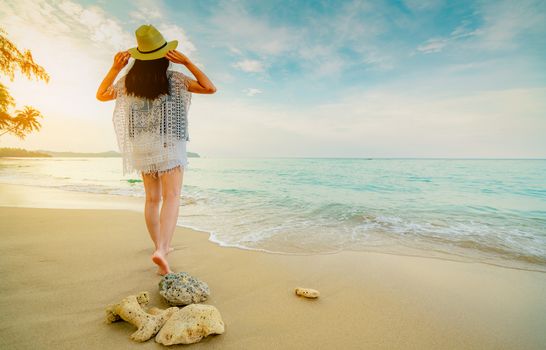 Happy young woman wear straw hat walking on the beach. Relaxing and enjoy holiday at tropical paradise beach with emerald green sea water. Girl in summer vacation. Summer vibes. Dead corals on beach. 