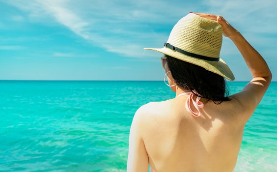 Back view of sexy young Asian woman wear pink bikini, straw hat, and sunglasses relaxing and enjoy holiday at tropical paradise beach. Girl in summer vacation fashion. Beauty sexy model. Summer vibes.