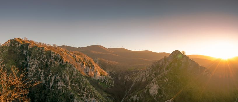 Landscape of mountain in the morning with sun light. Wind turbine on the top of mountain. Renewal energy. Green energy concept. Hill in spring season in Europe. Wind mill in a line on top of hill.