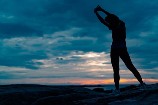 Silhouette woman workout in the morning at stone beach with beautiful sunrise sky. Fit woman stretching body before workout. Exercise for healthy lifestyle. Out door workout. Nature landscape. Freedom