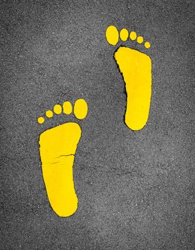 Yellow footprint painted on asphalt road. Walkway lane traffic sign. Foot mark on street texture background. Direction sign. Yellow footstep on tarmac floor. One step towards a better future concept.