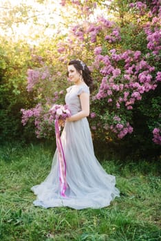 portrait of a brunette girl in a lilac spring garden before the wedding ceremony