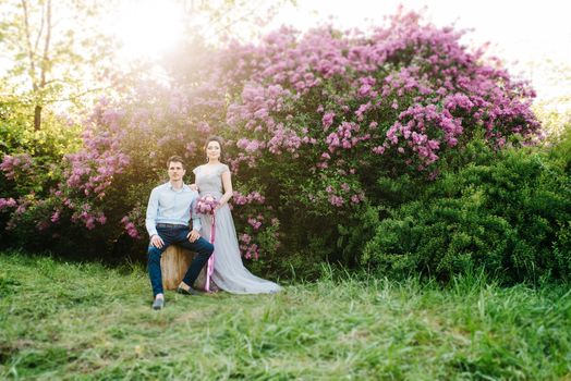 a guy and a girl walk in the spring garden of lilacs before the wedding ceremony