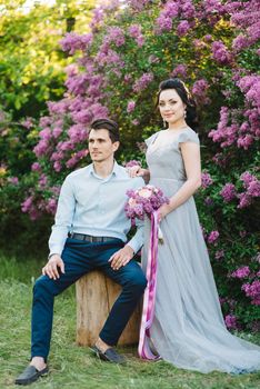 a guy and a girl walk in the spring garden of lilacs before the wedding ceremony