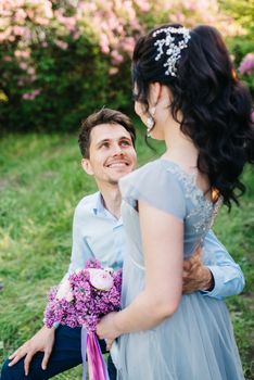 a guy and a girl walk in the spring garden of lilacs before the wedding ceremony