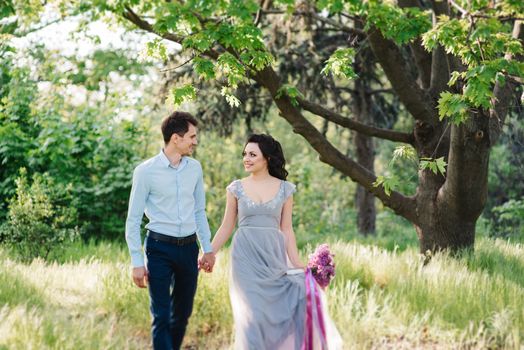 a guy and a girl walk in the spring garden of lilacs before the wedding ceremony