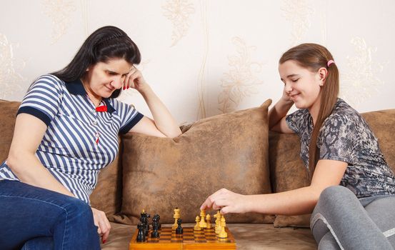 mom and daughter play chess while sitting on a sofa at home. coronavirus quarantine
