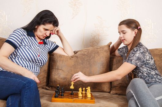 mom and daughter play chess while sitting on a sofa at home. coronavirus quarantine