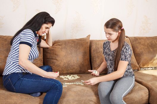 mom and daughter play dominoes while sitting on a sofa at home. coronavirus quarantine