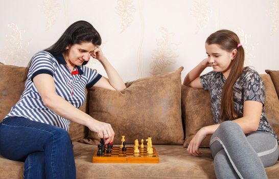 mom and daughter play chess while sitting on a sofa at home. coronavirus quarantine