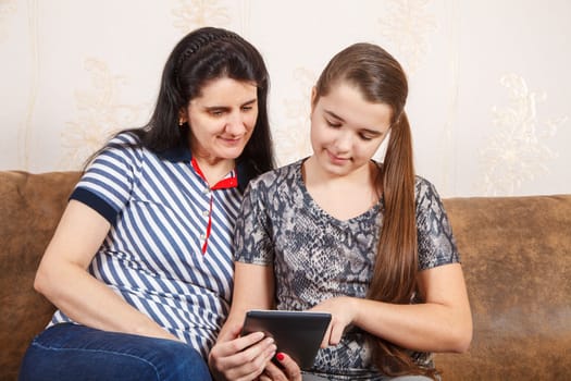 mom and daughter look at the tablet display while sitting on a sofa at home. coronavirus quarantine.