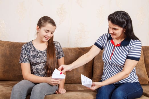 mom and daughter make paper boats while sitting on the sofa at home. coronavirus quarantine