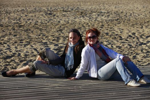 Two girls sits on the wooden bridge at beach
