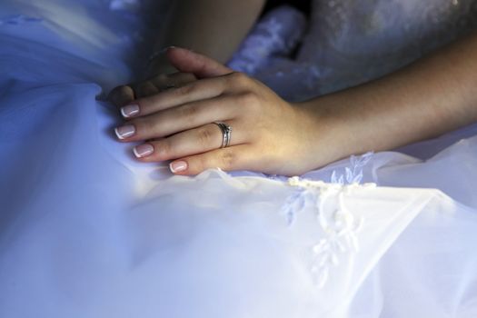 Hands of the bride on a background of a wedding dress.