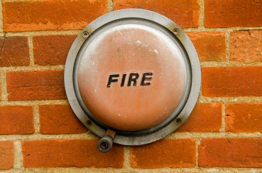 An old fashioned hand operated fire alarm bell fixed the brick wall of the exterior of a building.