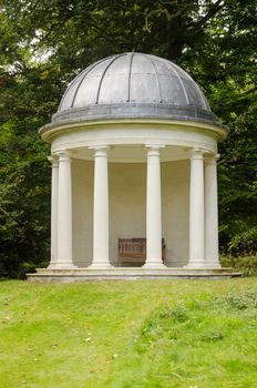 The historic Rotunda with doric columns and a garden bench set in the grounds of Bushy House, once home to King William IV and Queen Charlotte. Historic building, open to the public and hundreds of years old.