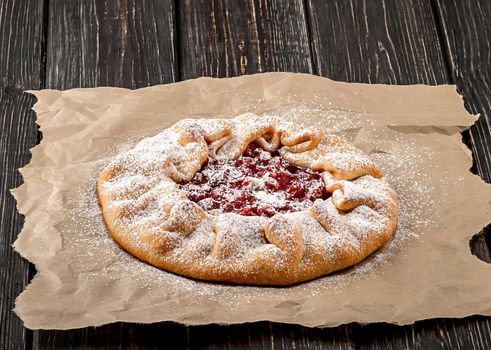 Galetta open gooseberries pie on crumpled paper and wooden table. Dusted with powdered sugar.