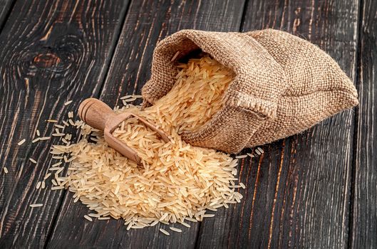 Sack with long rice and spoon lies on wooden background