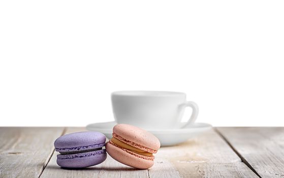 Two macaroons with a cup coffee on a wooden table isolated on white background