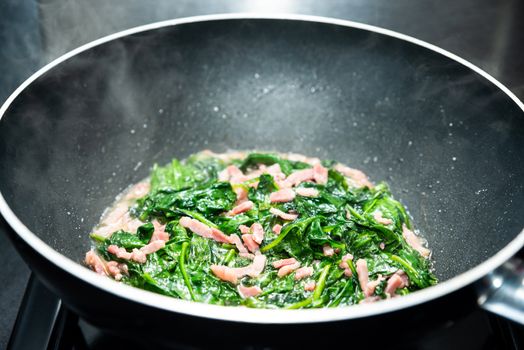 Cooking spinach with diced bacon in nonstick wok