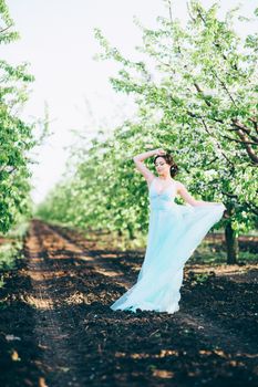 brunette girl in a turquoise dress walking in the spring garden