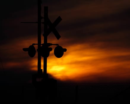 A silhouette of a rail crossing signal and sign before a vibrant orange sunset.
