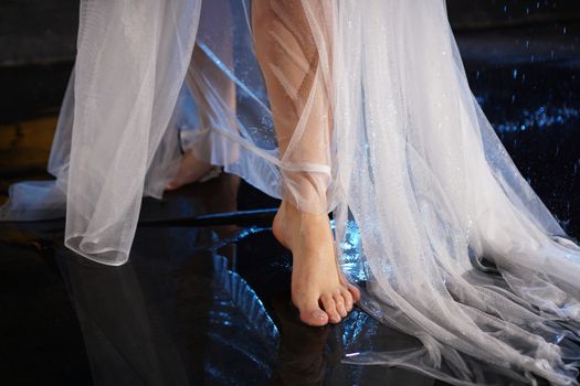 Beautiful female feet in the water with splashes. Photo in a neon light in the studio. White veil or long dress