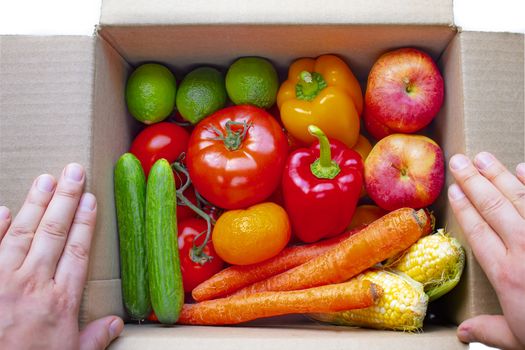 A person opening a deliver cardboard box with produce, fruits and vegetables inside on a white background