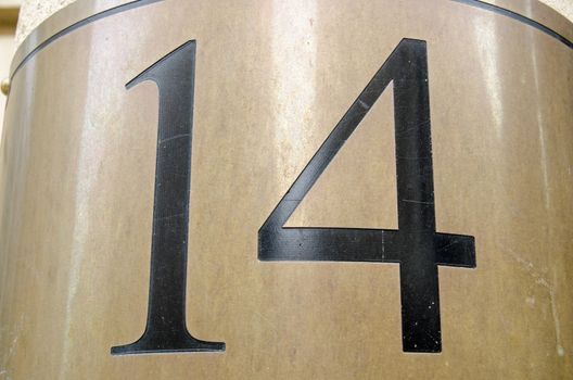 Figures for the number 14 incised into a curved brass plate outside an office block in central London. Viewed from public pavement.