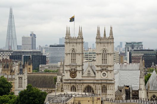 View across the rooftops towards the great West facade of the historic Westminster Abbey in London with the modern ladmaks of the Shard and Canary Wharf in the background.
