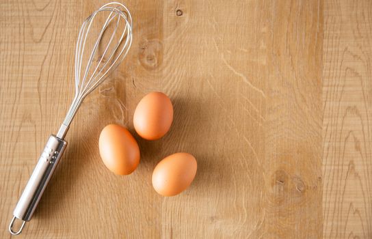 Chicken eggs and egg beater on wooden background.