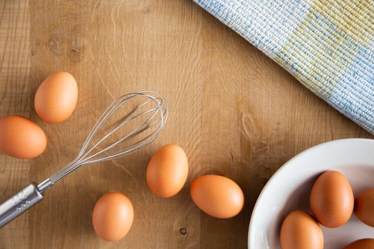 Chicken eggs and egg beater on wooden background.