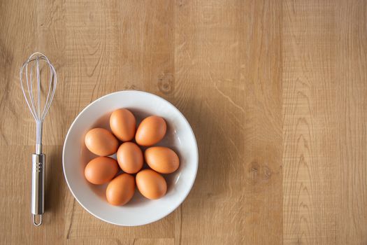 Chicken eggs and egg beater on wooden background.