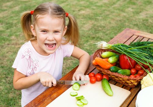 Little girl cutting vegetable for salad. Concept of healthy food.