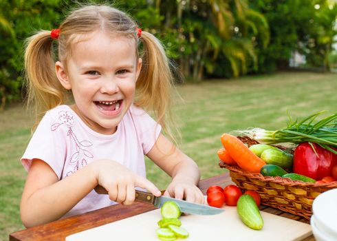 Little girl cutting vegetable for salad. Concept of healthy food.