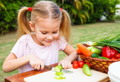 Little girl cutting vegetable for salad. Concept of healthy food.