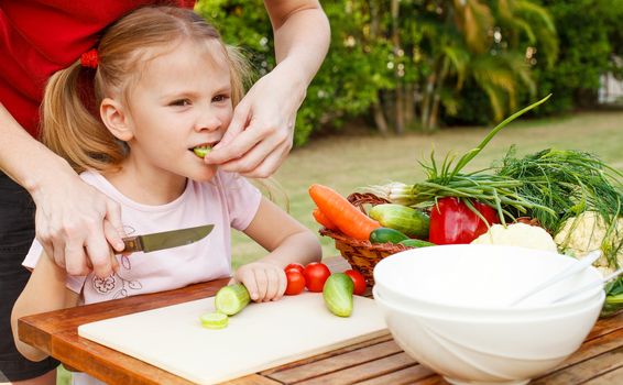 mother teaches daughter  knife cut cucumber